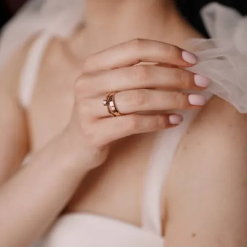 Mão da noiva com aliança e anel de noivado de ouro ajustando o laço do vestido